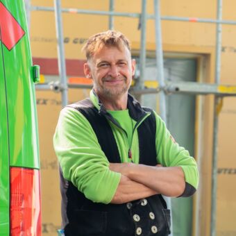 Porträtfoto Gunnar - Er steht auf einer Baustelle neben dem Firmenfahrzeug