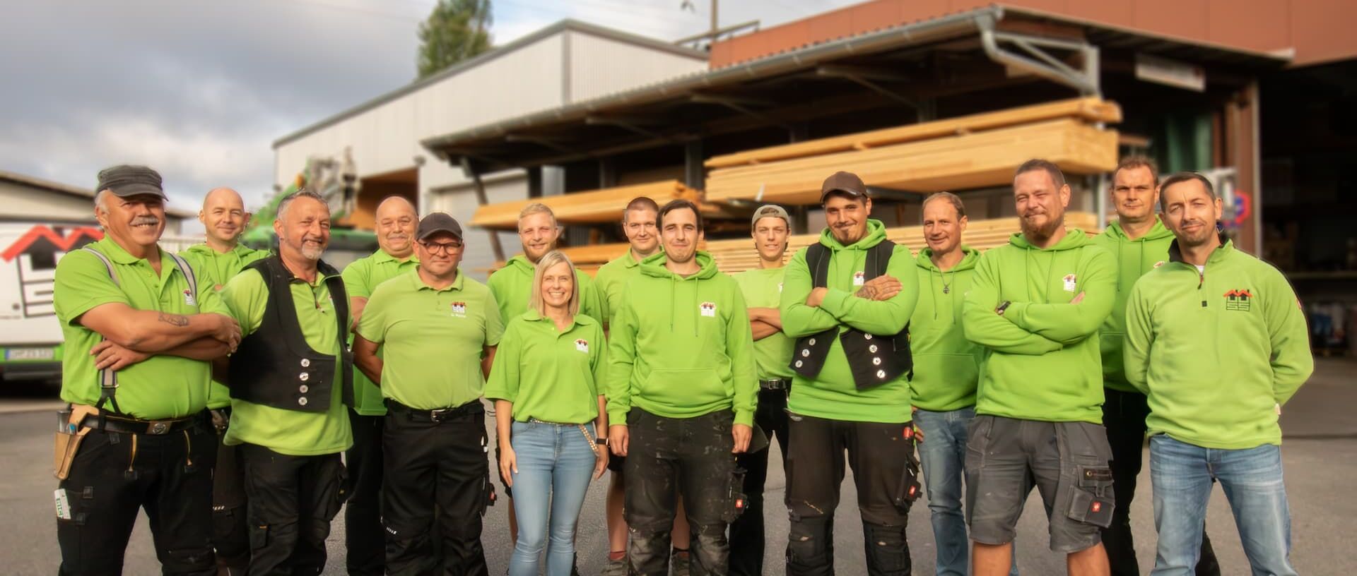 Das Team von Heiko Muuss steht nebeneinander auf dem Firmengelände. Im Hintergrund aufeinander gestapeltes und geordnetes Holz.