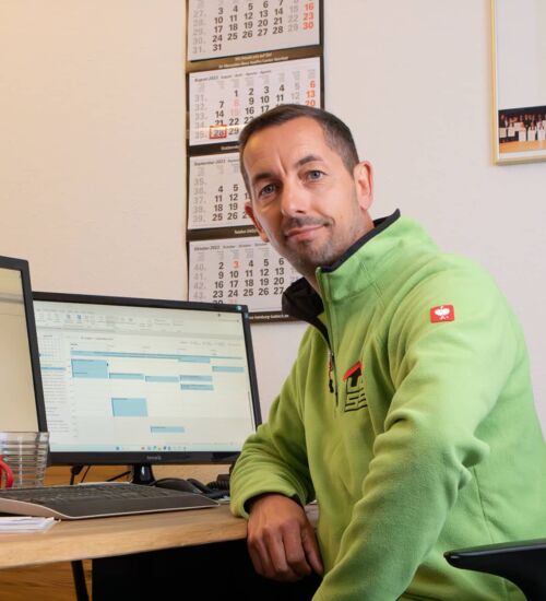 Der Geschäftsführer Carsten Pichura sitzt am Bürotisch, auf dem zwei Bildschirme stehen.