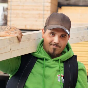 Porträtfoto Christopher - Auf seiner Schulter trägt er drei Holzlatten