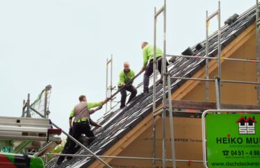 Mitarbeiter helfen sich gegenseitig, die Photovoltaik-Platten auf das Dach zu bekommen.