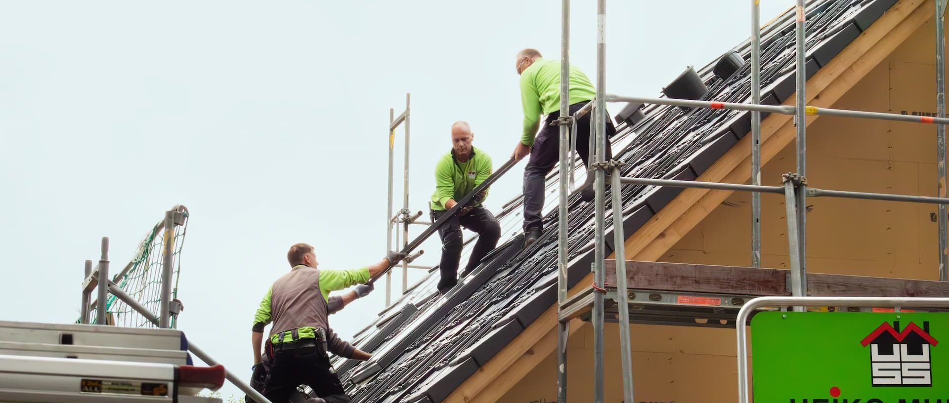 Auf dem Dach Mitarbeiter helfen sich gegenseitig, die Photovoltaik-Platten auf das Dach zu bekommen.