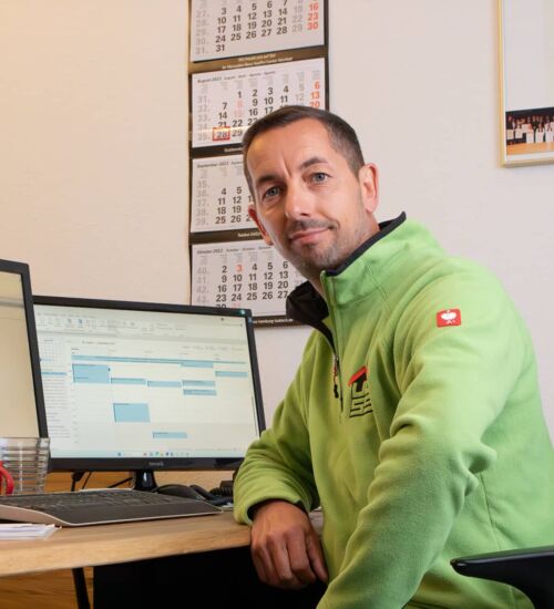 Terminierung des Auftrags Der Geschäftsführer Carsten Pichura sitzt am Bürotisch, auf dem zwei Bildschirme stehen.